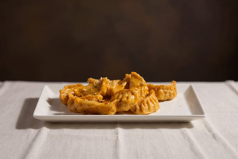 A white rectangular plate filled with golden-brown dumplings, sprinkled with sesame seeds, on a white tablecloth.